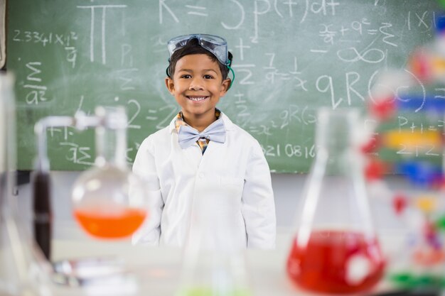 Smiling schoolboy standing in classroom with chemical flask in foreground