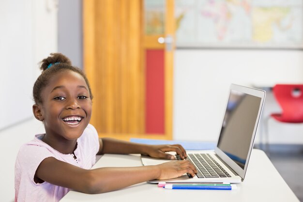 Smiling schoolgirl using laptop in classroom