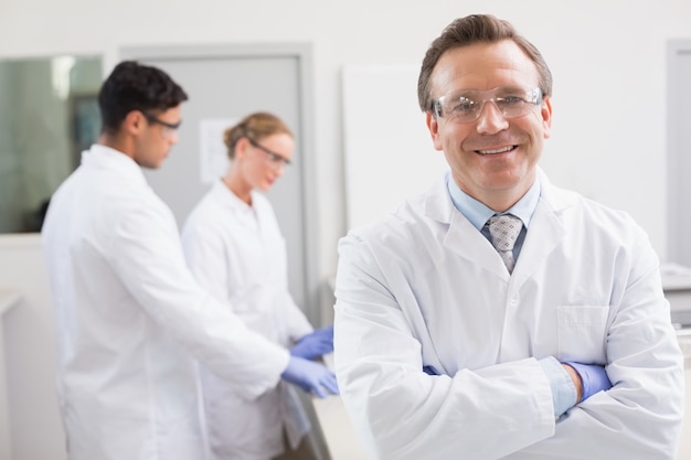 Smiling scientist looking at camera while colleagues working behind 