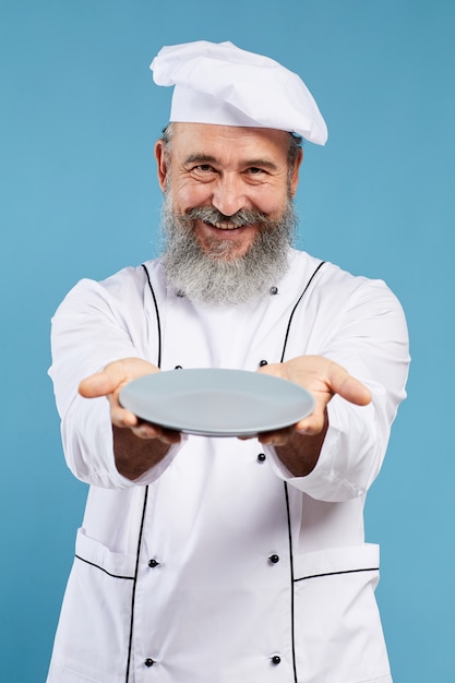 Smiling Senior Chef Holding Empty Plate on Blue