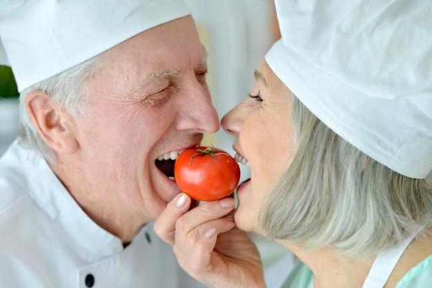smiling Senior chefs couple with tomato  at kitchen