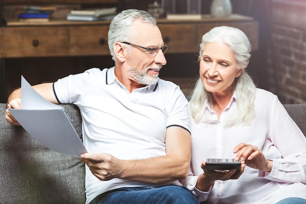 Улыбающаяся пожилая пара рассчитывает свои финансовые последствия дома