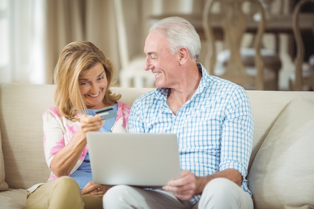 Улыбающаяся старшая пара делает покупки в Интернете на ноутбуке в гостиной