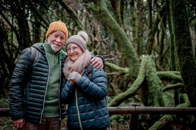 Smiling senior couple enjoying nature outdoors walking in a mountain forest with moss covered trunks Cheerful elderly couple traveling together in Garajonay national park of La Gomera