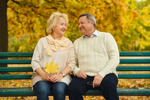 Smiling senior couple sitting on the bench in the park together enjoying retirement