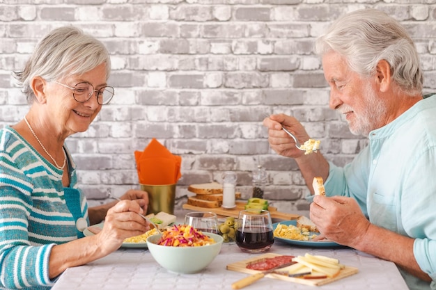 고요한 은퇴 후 집에서 함께 브런치를 먹으면서 집 테이블에 얼굴을 맞대고 앉아 웃고 있는 노부부