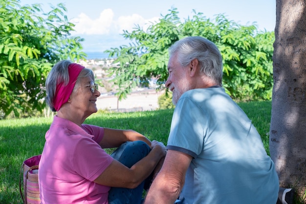 Улыбающаяся пожилая пара, сидящая в парке, отдыхающая вместе на пенсии