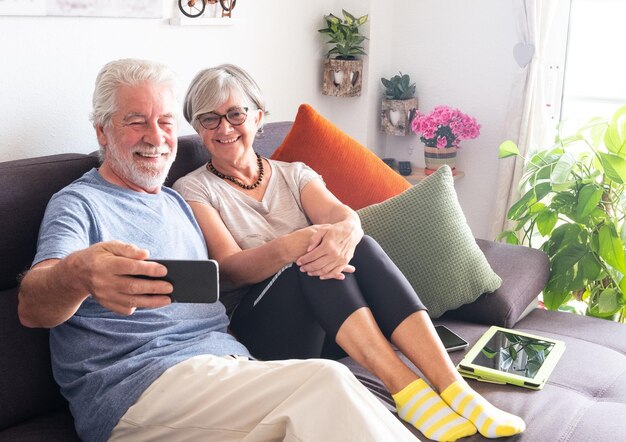 Smiling senior couple taking selfie while sitting on sofa at home