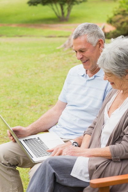 Улыбаясь старший пара, используя ноутбук в парке