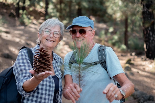 Smiling senior couple with backpacks looks in camera while enjoying a mountain hike in the woods