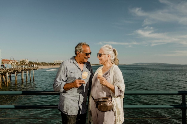 Улыбающаяся старшая пара с рожком мороженого, стоящая на пирсе Санта-Моники