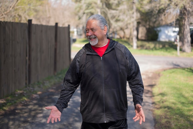 Photo smiling senior man gesturing while standing on footpath at park