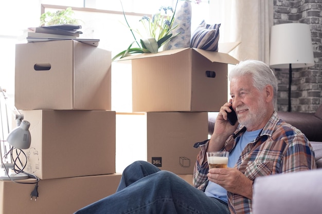 Photo smiling senior man on moving day sitting on floor browsing with smartphone talking on cell