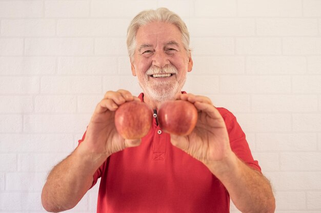 Smiling senior man in red isolated over a white background holding two red apples fruit in hands