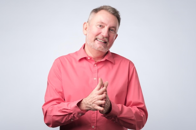 Smiling senior man in redl clothes standing and rubbing palms