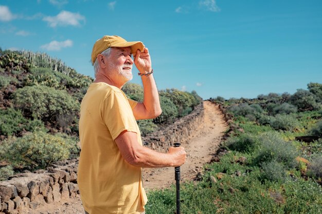 Photo smiling senior man walking in a sunny day on trail outdoors on mountain excursion relaxed caucasian man enjoying travel or retirement leading healthy lifestyle