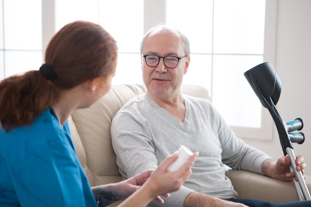 Smiling senior man with crutches in nursing home and female doctor with pills