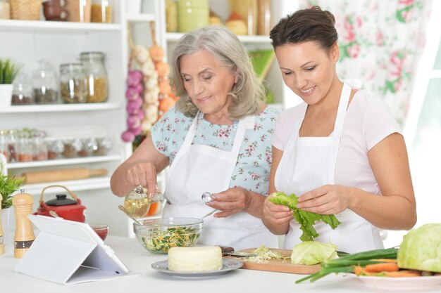 Smiling senior mother and adult daughter cooking together