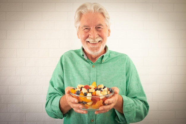 Smiling senior whitehaired man ready to eat a salad of fresh summer fruits Breakfast or lunch time healthy eating