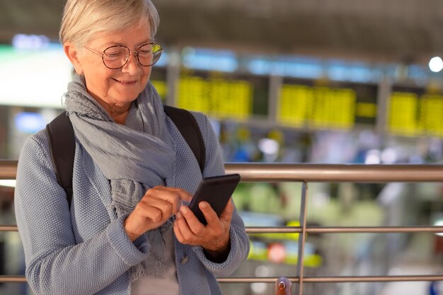 Photo smiling senior woman in aeroport waiting for boarding using mobile phone connection to send messages