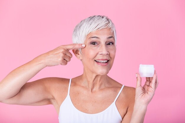 Photo smiling senior woman applying antiaging lotion to remove dark circles under eyes mature woman using cosmetic cream to hide wrinkles lady using day moisturizer to counteract the aging of the skin