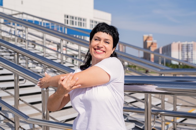 Smiling senior woman doing stretching outdoors on urban scene