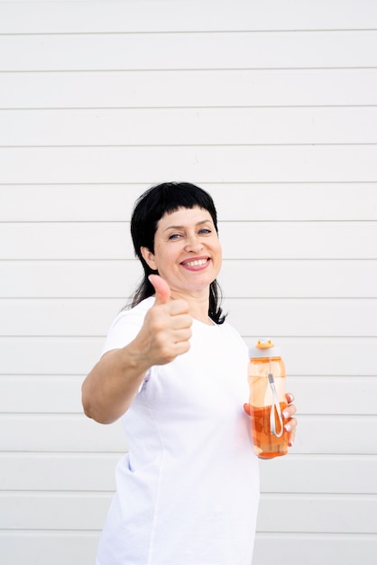 Smiling senior woman drinking water after workout outdoors on urban scene