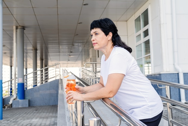 Smiling senior woman drinking water after workout outdoors