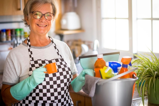 家のキッチンの容器のそばに立ってコーヒーを飲んでいる笑顔の高齢の女性