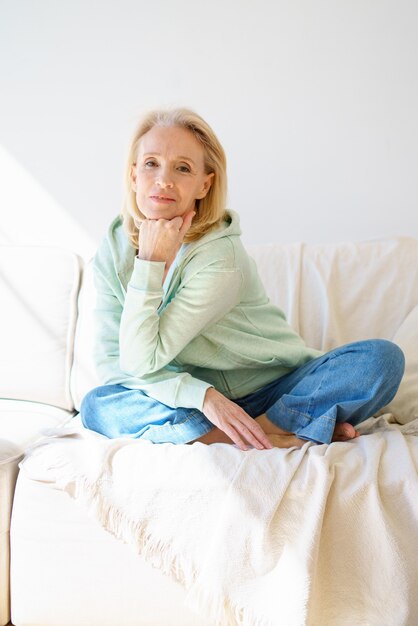 Smiling senior woman looking at camera and relaxing on sofa in daytime at home