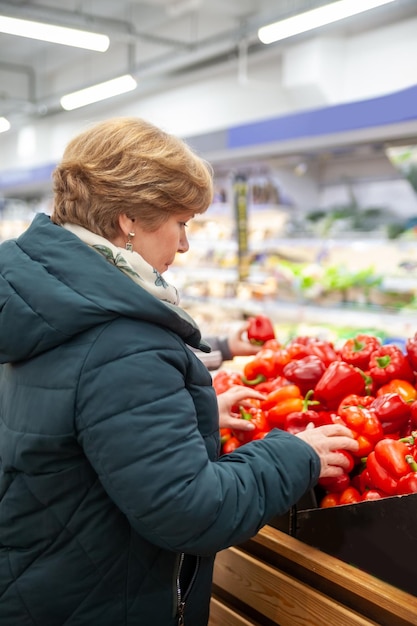 Улыбающаяся пожилая женщина собирает яблоко в продуктовом магазине