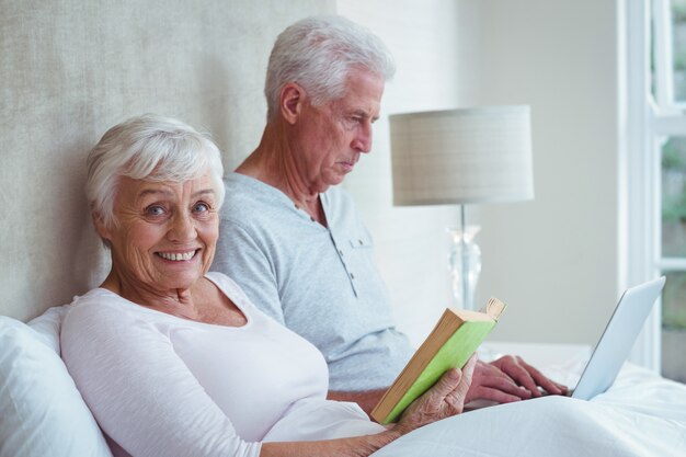 Smiling senior woman reading book while man using laptop 