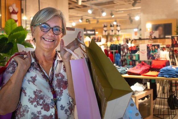 Smiling senior woman satisfied with purchases in a mall loaded with shopping bags