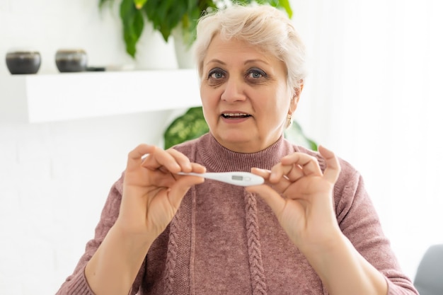 Smiling senior woman shows thermometer.