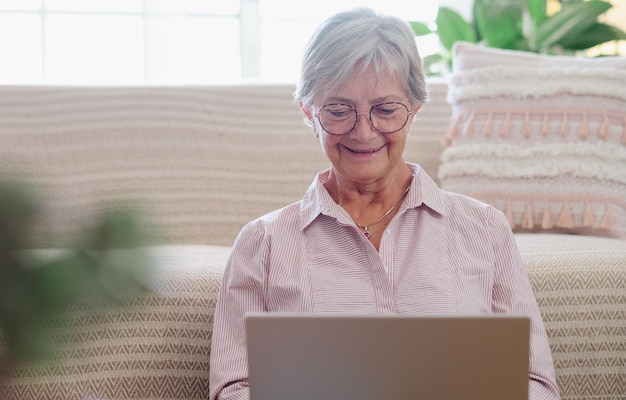 Photo smiling senior woman sitting on the floor at home while browsing on laptop enjoying technology