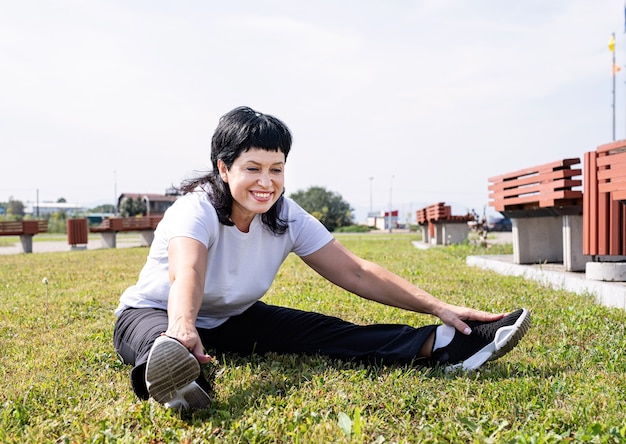 Smiling senior woman warming up stretching outdoors in the park