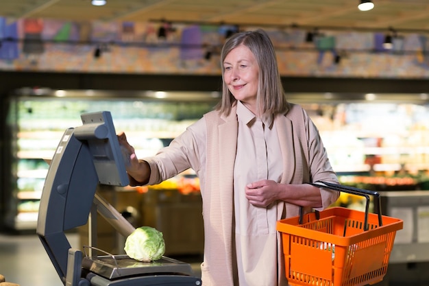 Smiling senior woman weighs vegetables in supermarket