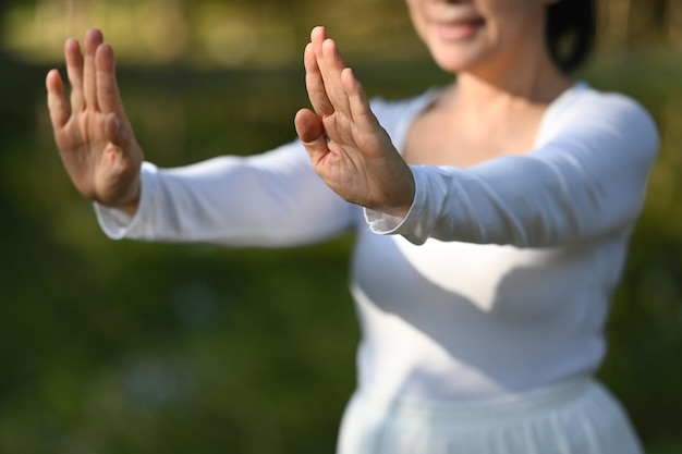 Donna anziana sorridente in abiti bianchi che pratica tai chi nel parco concetto di assistenza sanitaria