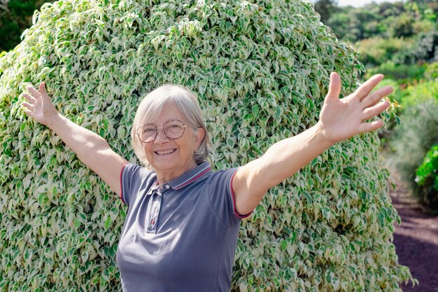Foto una donna anziana sorridente con le braccia aperte che si gode una giornata di sole in un bellissimo giardino