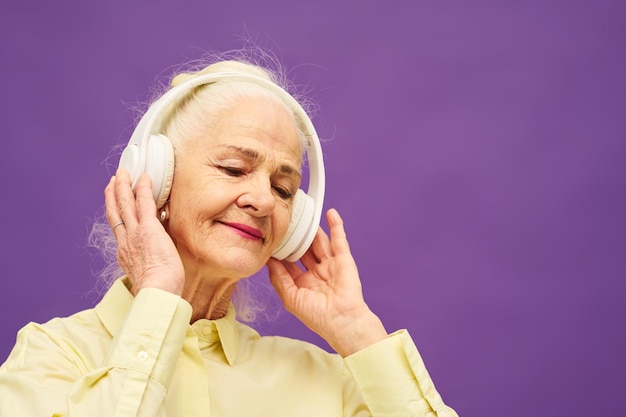 Smiling senior woman with white hair touching headphones while enjoying music