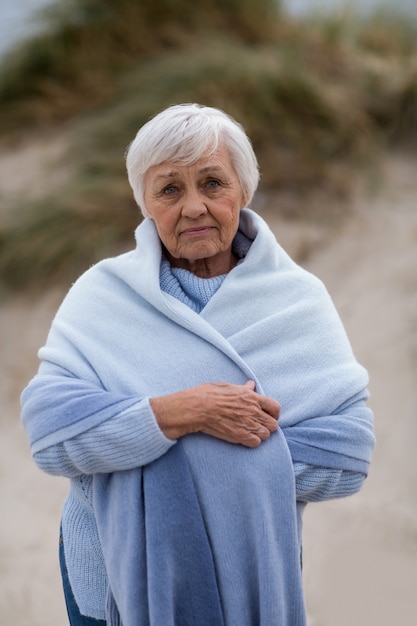 Smiling senior woman wrapped in shawl at beach