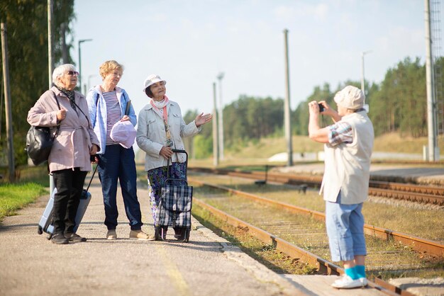 笑顔の高齢の女性が電車が出発するのを待っているプラットフォームで写真を撮る