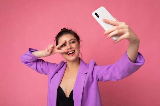 Улыбаясь сексуальная красивая взрослая женщина в фиолетовом костюме, делающая селфи фото на мобильном телефоне