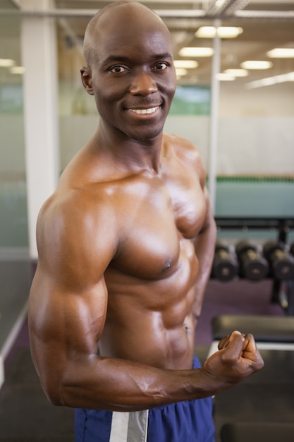 Smiling shirtless muscular man posing in gym