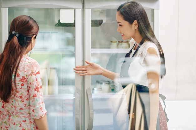 Улыбающийся продавец показывает покупателям холодильники с молочными продуктами без лактозы и свежими йогуртами