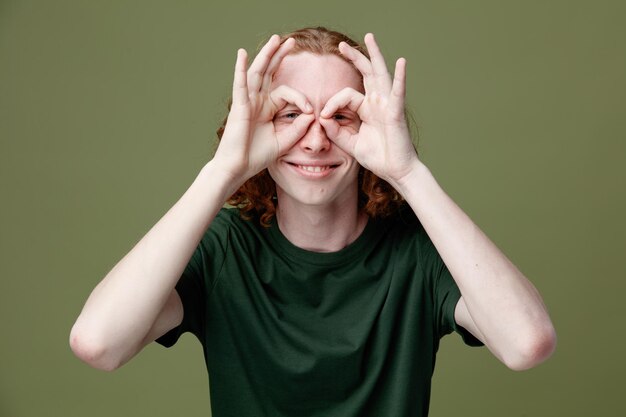 Sorridente che mostra gesto giovane bel ragazzo che indossa una maglietta verde isolata su sfondo verde