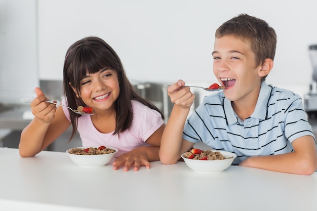 Smiling siblings eating cereal for breakfast in kitchen 