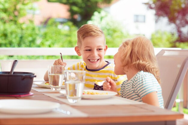 Foto fratelli sorridenti che fanno colazione al tavolo nel cortile