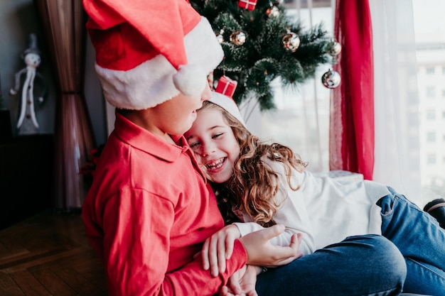 Foto fratelli e sorelle sorridenti che indossano cappelli di babbo natale mentre sono a casa