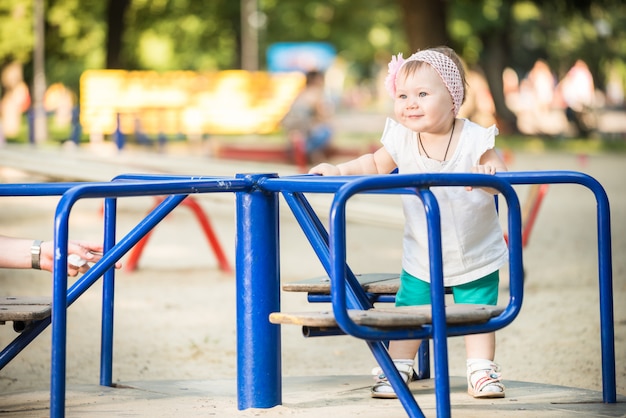 Smiling small baby girl standing and riding carousel at playground